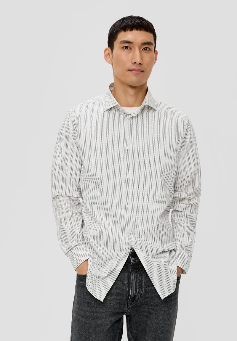 Weißes Hemd mit kleinen schwarzen Pünktchen, langen Ärmeln und spitzem Kragen, kombiniert mit dunklen Denim-Jeans.
