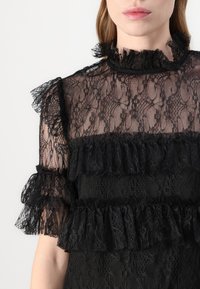Vestito nero in pizzo con maniche arricciate e dettagli in pizzo a strati. Il tessuto è trasparente con motivi intricati e un design a collo alto.