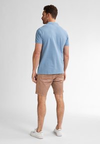 Lichtblauwe polo, korte mouwen, met een rechte snit; gecombineerd met tan shorts, met zijzakken en een relaxte pasvorm; witte sneakers.