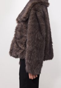 Veste en fausse fourrure grise à coupe carrée, manches larges et texture douce. Dotée d'un col châle et sans fermetures visibles.