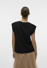 Top nero a maniche corte con vestibilità rilassata. Indossato sopra una gonna in tulle beige a strati, che presenta una texture soffice e un design fluido.