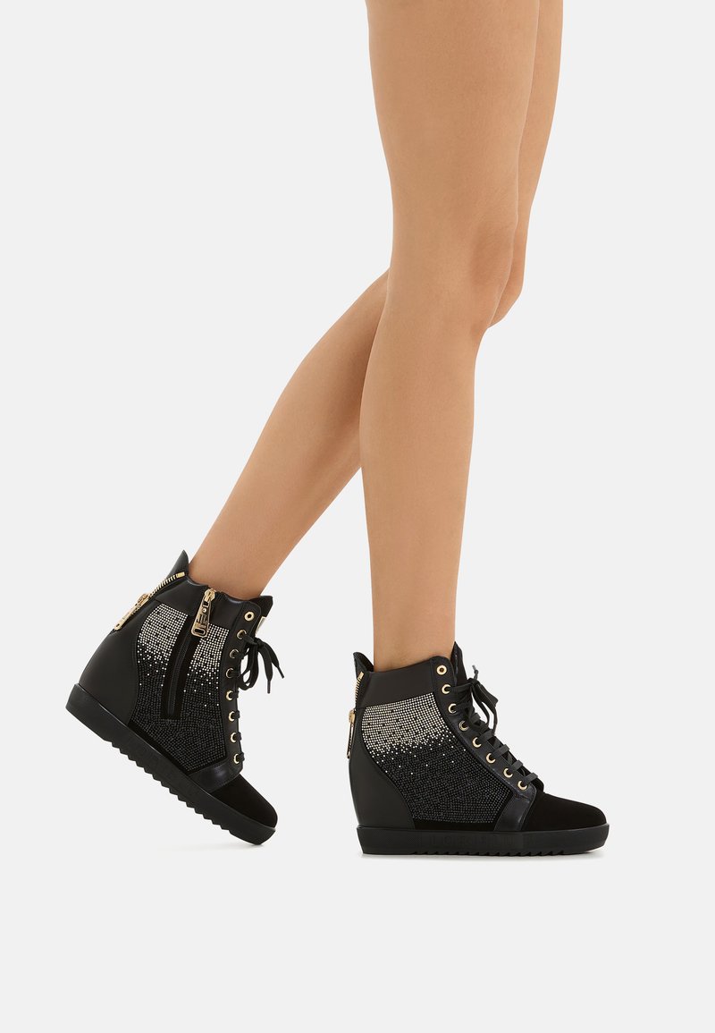 Sneakers a zeppa nera con una parte superiore in tessuto testurizzato, dettagli metallici, una cerniera laterale e chiusura con lacci. Presentano un design a gradiente di glitter.