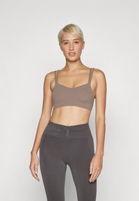 Bralette de tela suave marrón con tirantes delgados dobles y un escote redondeado; combinado con leggings grises de cintura alta con un detalle fruncido.
