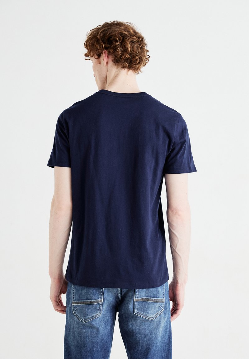 Camiseta de algodón azul marino de manga corta, con cuello redondo y corte relajado, combinada con jeans azul claro que tienen costuras en los bolsillos traseros.