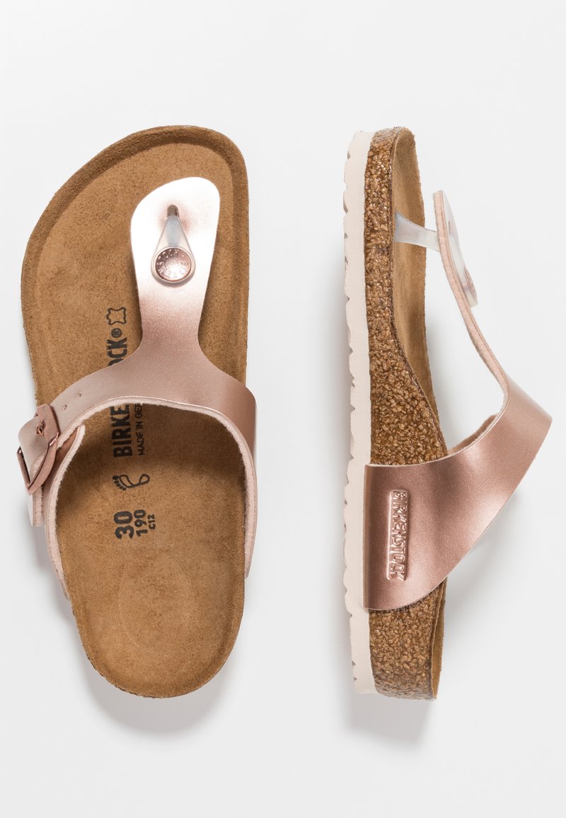 Infradito Birkenstock color oro rosa con una fascia metallica liscia, soletta in finta suede imbottita e suola in sughero testurizzato. Dettaglio con fibbia regolabile.