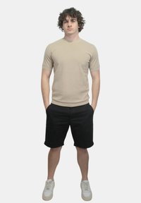 T-shirt fitted a maniche corte beige abbinato a pantaloni corti neri e sneakers bianche. La t-shirt presenta un collo rotondo e una texture liscia.
