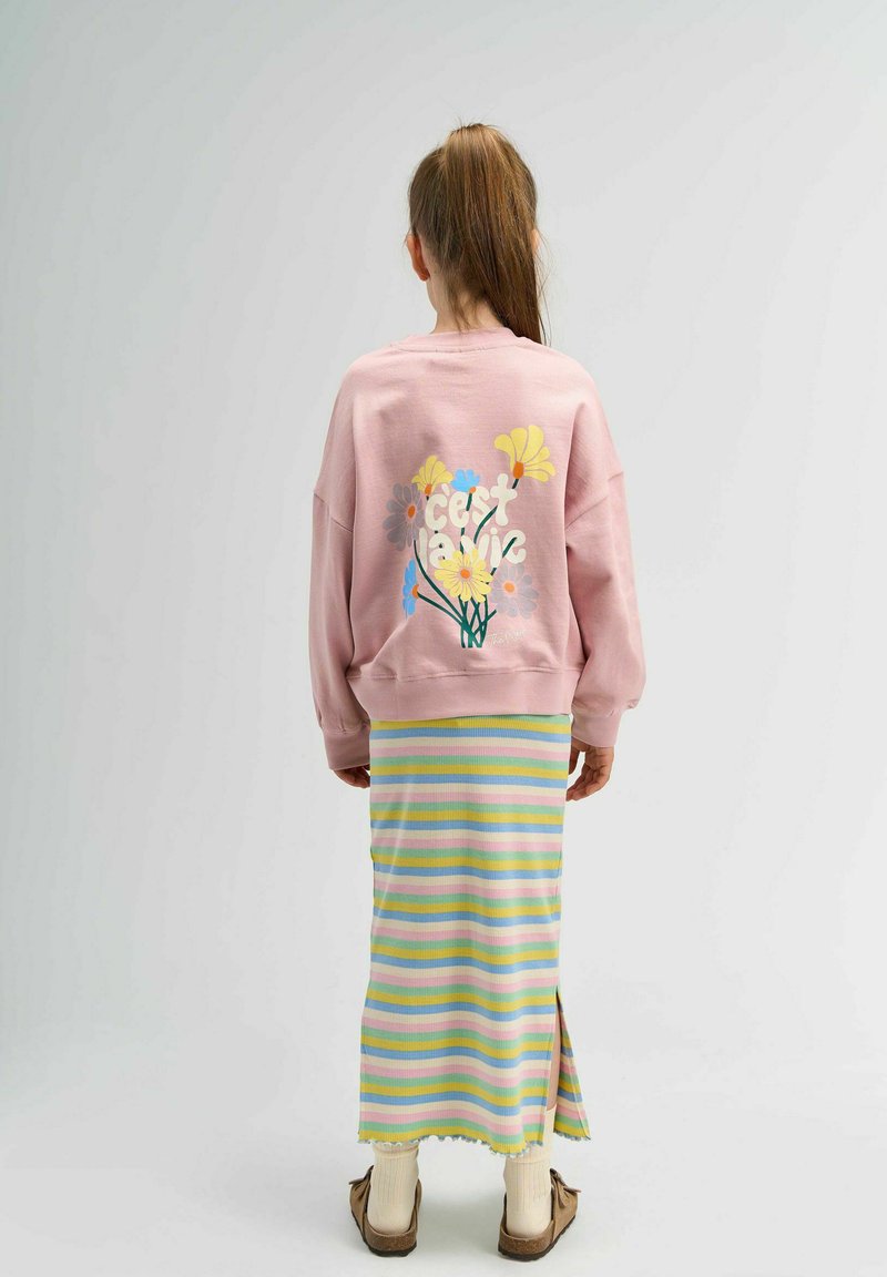 Sweatshirt rose avec imprimé floral et texte "c'est la vie" au dos ; associé à une jupe rayée multicolore et des chaussures marron à enfiler.