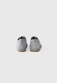 Une paire de chaussures en daim grises vue de l'arrière, semelles plates, sur un fond blanc uni.