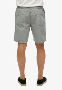 Shorts en coton gris avec une taille élastique, deux poches arrière et une coupe décontractée. Portés avec des chaussures noires à enfiler avec une semelle tissée.