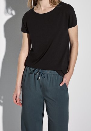 Schwarzes Kurzarm-T-Shirt, kombiniert mit dunkelgrünen Kordelzughosen, die einen lässigen Schnitt und eine weiche Stofftextur betonen.