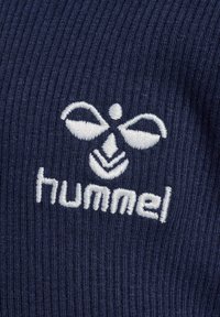 Marinefarbener Rippenstoff mit einem weißen gestickten Logo, das ein Bienenmotiv zeigt, darunter das Wort "hummel". Es hebt die Textur und den Kontrast hervor.