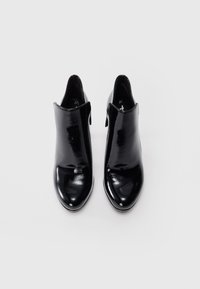 Bottines en cuir verni noir avec un bout rond et un design découpé. Taille 37, texture lisse, matériel minimal, apparence élégante.