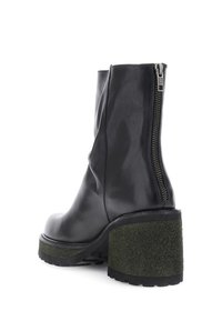 Botín negro de cuero hasta el tobillo con un tacón de bloque verde texturizado. Cuenta con una cremallera lateral y una superficie lisa, destacando un diseño moderno.