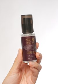 Bottiglia di vetro trasparente con un tappo a pompa marrone scuro; contiene un siero viola; l'etichetta include testo sugli ingredienti e le istruzioni; dimensione di 35 ml.