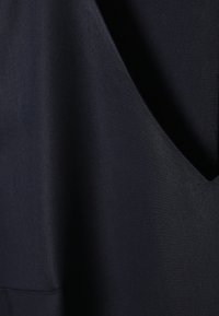 Detailní záběr hladké tmavě modré tkaniny s jemnými záhyby a subtilní diagonální strukturou vazby.