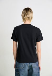 Schwarzes Baumwoll-T-Shirt mit kurzen Ärmeln und Rundhalsausschnitt, mit regulärem Schnitt. Getragen mit Denim-Cargo-Hosen, einfarbiger Hintergrund.