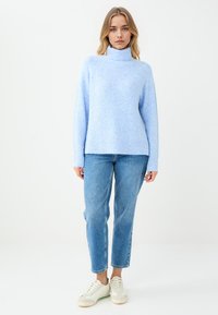 Helles blaues Woll-Turtleneck mit lockerer Passform und gerippten Bündchen, kombiniert mit blauen Jeans im Straight-Leg-Schnitt und weißen Sneakern.