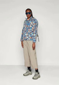 Färgglad mönstrad pulloverjacka med dragkedja i kragen, blå och peach toner. Matchad med beige capribyxor och grå sneakers.