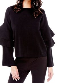 Schwarzer gestrickter Pullover mit Rüschensleeves und rundem Ausschnitt. Der Stoff hat eine gerippte Textur, kombiniert mit engen schwarzen Hosen.