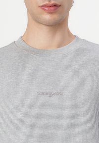 Gray waffle-knit sweatshirt featuring a crew neckline and embroidered logo in a subtle tone on the chest. Textured fabric detail visible.