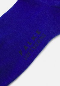Calzino in cotone blu con una superficie liscia e il marchio stampato in nero "FALKE SOFTNESS" vicino alla parte superiore. Design classico di calzino a crew.