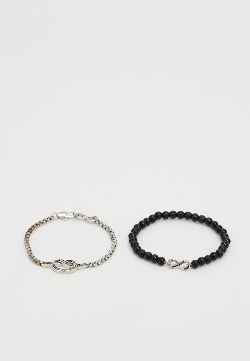 Due braccialetti: un braccialetto in catena d'argento con chiusura a nodo (sinistra) e un braccialetto con perline nere che presenta un simbolo di infinito (destra).