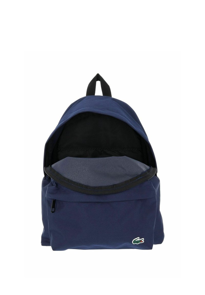 Navy blue backpack with open main compartment, front zip pocket, black top handle, and small green crocodile logo on front pocket.