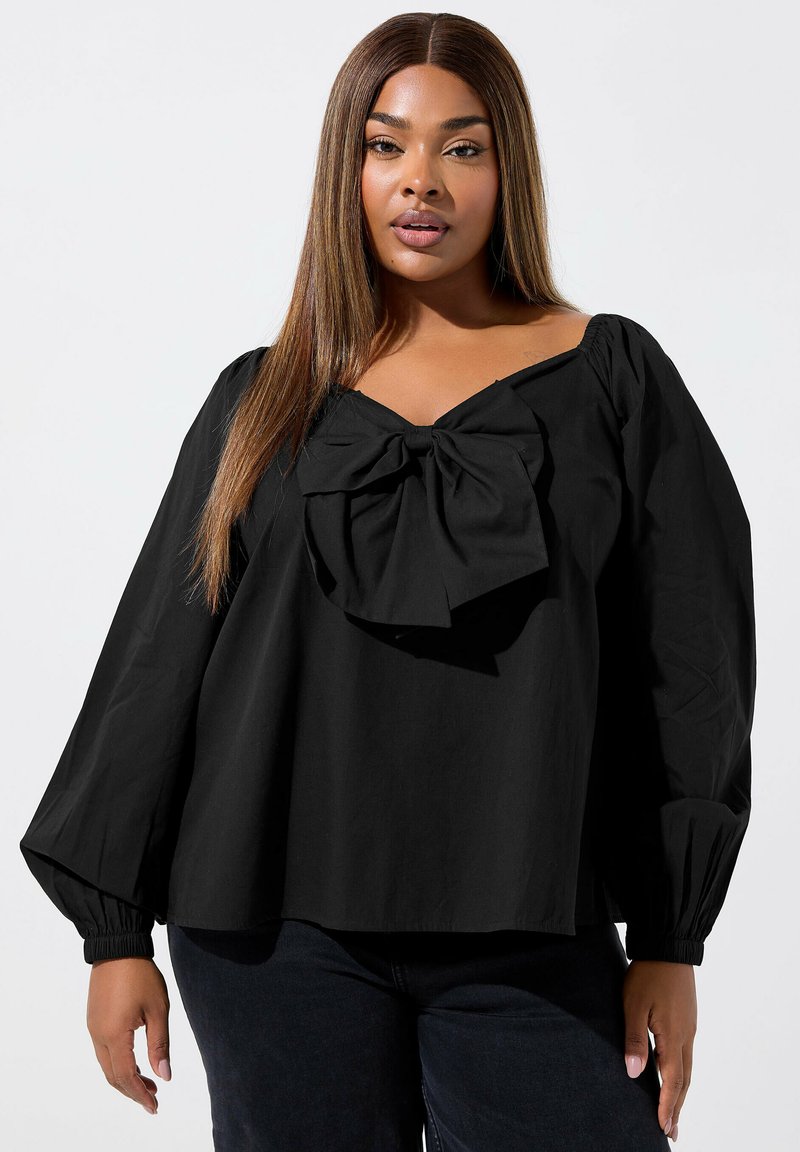 Svart blus med puffärmar och en stor rosett detalj vid halsringningen. Tillverkad av lättviktigt tyg, med en lös och avslappnad passform.