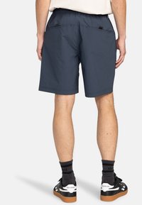 Marinblå shorts med elastiskt midjeband, två bakfickor och en avslappnad passform. Bärs med svarta sneakers och mönstrade strumpor.