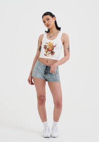 Camiseta sin mangas blanca con estampado colorido de mariposas y flores; pantalones cortos de mezclilla azul claro con cordones en la parte frontal y bordado de flores; zapatillas blancas.