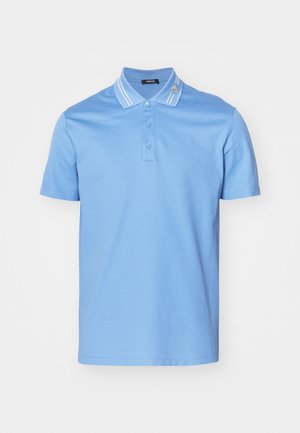 Camisa polo de color azul claro hecha de algodón, con una tapeta de tres botones, acentos de cuello a rayas y un pequeño emblema decorativo en el cuello.