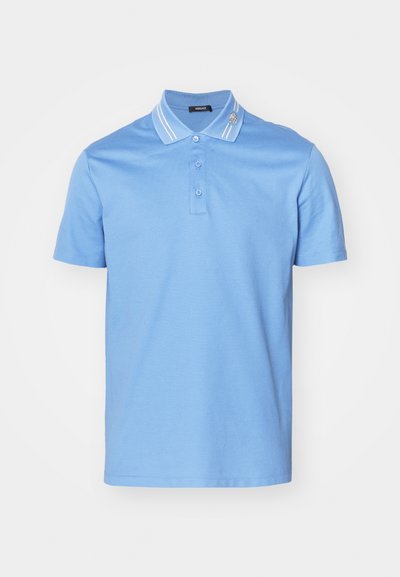 Polo azul claro feito de algodão, com uma pala de três botões, detalhes em listras na gola e um pequeno emblema decorativo na gola.