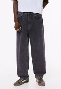 Dunkelviolette, weite Jeans aus Denim mit Fronttaschen und Knopfverschluss an der Taille, kombiniert mit grauen Sneakers.