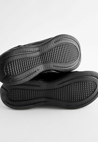 Black athletic shoes, featuring a textured rubber sole with a patterned grip and sleek design; smooth upper material extends to the heel.
