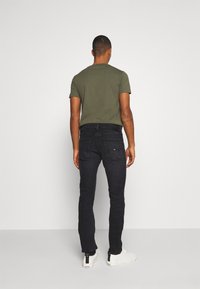 Svarta denimjeans med smal passform, i kombination med en åtsittande olivgrön t-shirt och vita sneakers; minimal design, inga påfallande mönster.