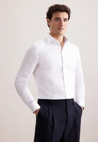 Witte overhemden met een getailleerd ontwerp, knoopsluiting aan de voorkant en een gemusterde kraag. Draagt met marineblauwe broek; gladde textuur, lange mouwen.