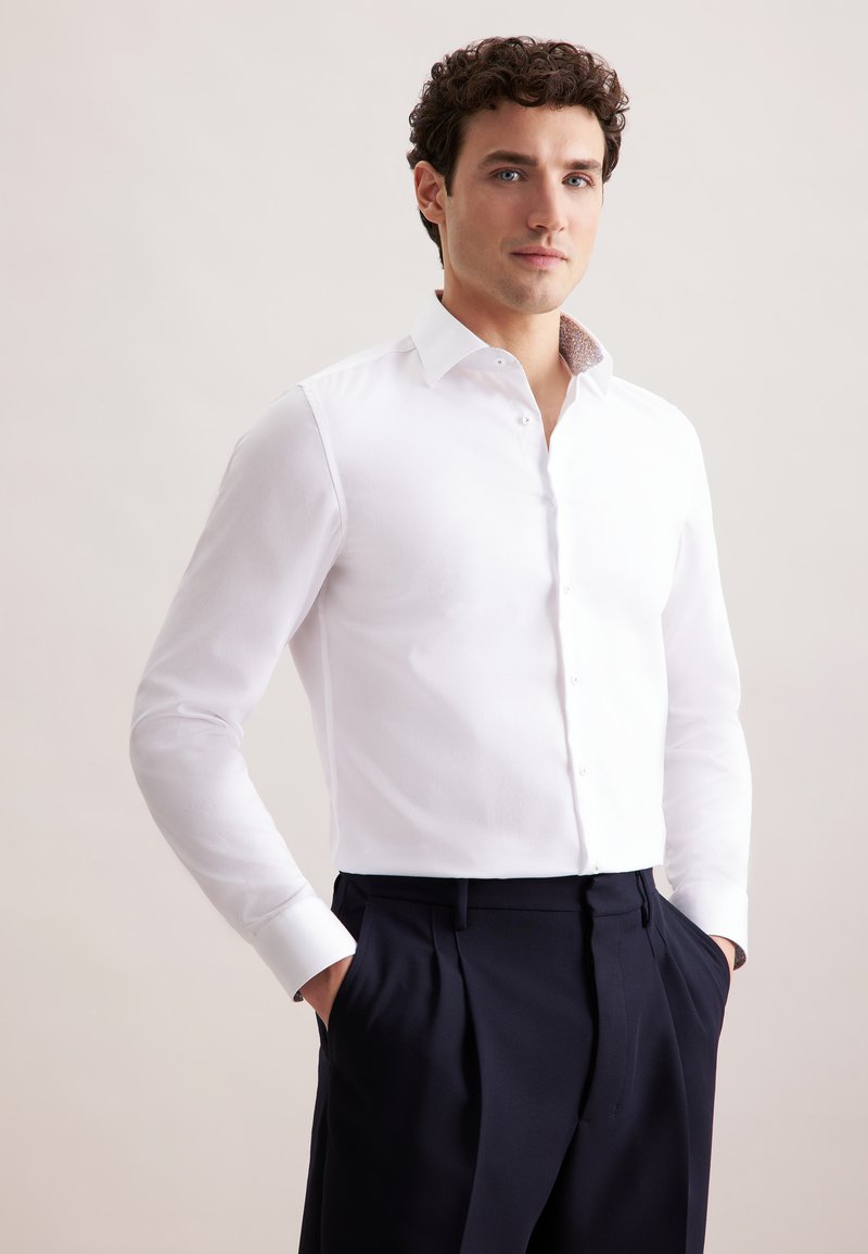 Witte overhemden met een getailleerd ontwerp, knoopsluiting aan de voorkant en een gemusterde kraag. Draagt met marineblauwe broek; gladde textuur, lange mouwen.