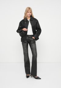 Črna usnjena jakna z ovratnikom, bela majica, temno sive kavbojke in črni čevlji z ostrim sprednjim delom. Gladek tekstura in oprijeta silhueta.