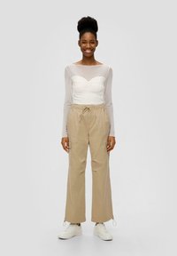 Witte lange mouwen top met gerimpelde halslijn, gecombineerd met beige cargobroek; broek heeft zakken en verstelbare manchetten; gedragen met witte sneakers.