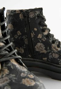 Bottines noires à motif floral, fabriquées en matériau texturé, avec une fermeture éclair sur le côté, des lacets et une semelle en caoutchouc robuste.