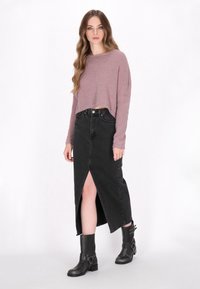 Roze cropped sweater, zwarte denim rok met een split aan de voorkant, gedragen met zwarte enkellaarsjes met metalen accenten.