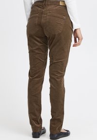 Rudi korduro kelnės, siaurėjančios formos, su dviem galiniais kišenėmis ir prekės ženklo etiketė ant juosmens. Lygus tekstūra ir juostuotas raštas.