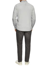 Helles graues Langarmhemd mit Button-down-Kragen. Getragen mit dunkelgrauen Hosen und weißen Sneakers, die eine glatte Textur und eine figurbetonte Passform aufweisen.