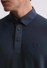 Granatowa, prążkowana koszulka polo z zapinanym na guziki dekoltem, kontrastowym kołnierzykiem oraz małym haftowanym logo na piersi. Teksturowana tkanina.