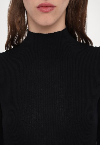 Svart ribbat turtleneck med hög krage och långa ärmar, med ett strukturerat stickat mönster. Närbild, inga ytterligare detaljer.