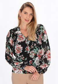 Blusa floreale con base nera, caratterizzata da grandi fiori rosa e verdi. Maniche lunghe e gonfie e scollatura a V, con chiusura a bottoni.