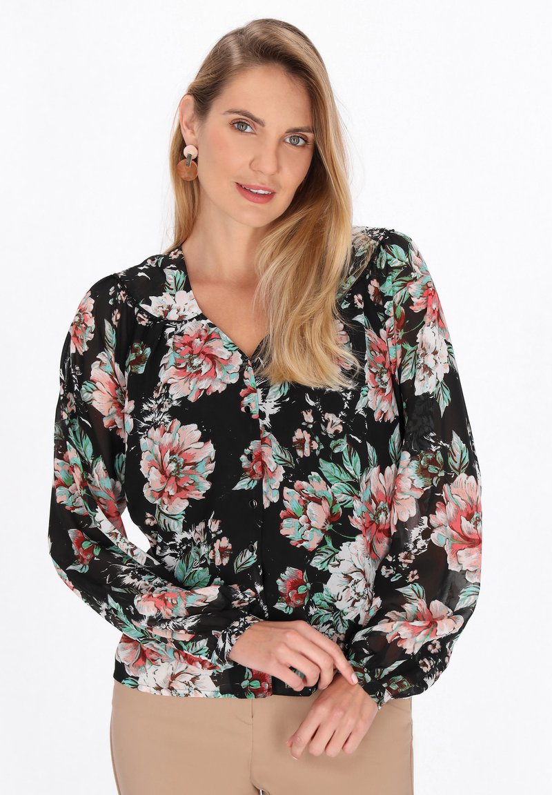 Blusa floreale con base nera, caratterizzata da grandi fiori rosa e verdi. Maniche lunghe e gonfie e scollatura a V, con chiusura a bottoni.