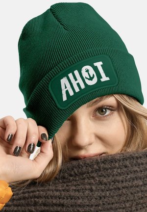 Green knitted beanie featuring a rectangular patch with the word "AHOI" and an anchor graphic in white. Textured ribbed design.