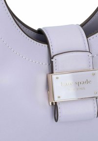 Lavendel leren handtas met een brede strap en een gouden metalen plaat met de merknaam. Gladde textuur en subtiele stiksels.