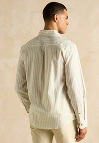 Ribaga kerge beež särk, mis on valmistatud tekstuursematerjalist, väike krae, nööbitud mansetid ja selja lõhiku detail.